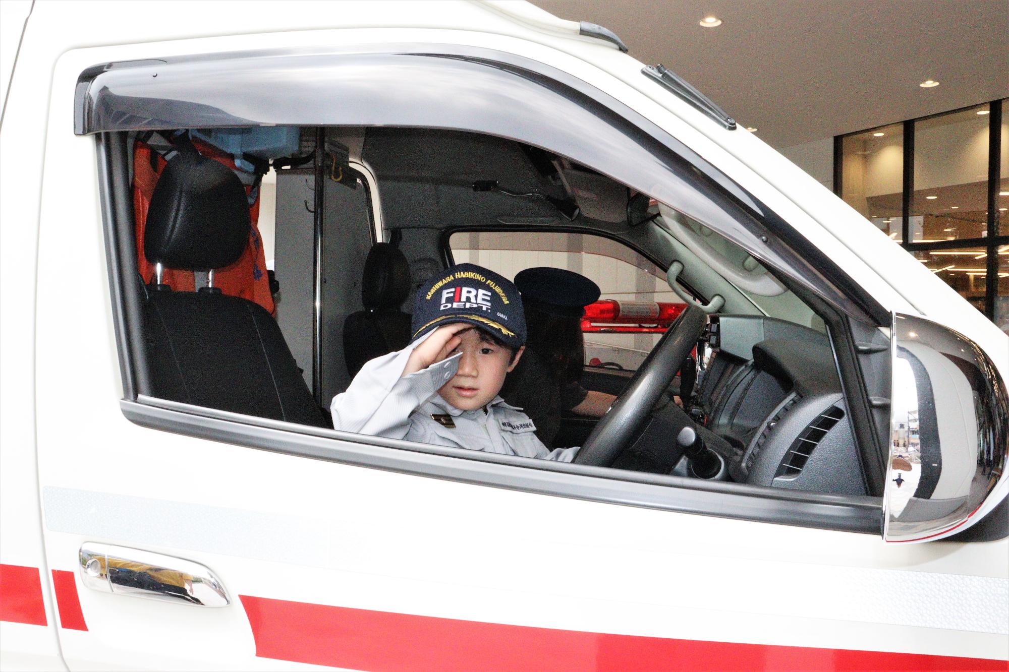 子供が救急車の運転席に乗車して記念撮影している様子