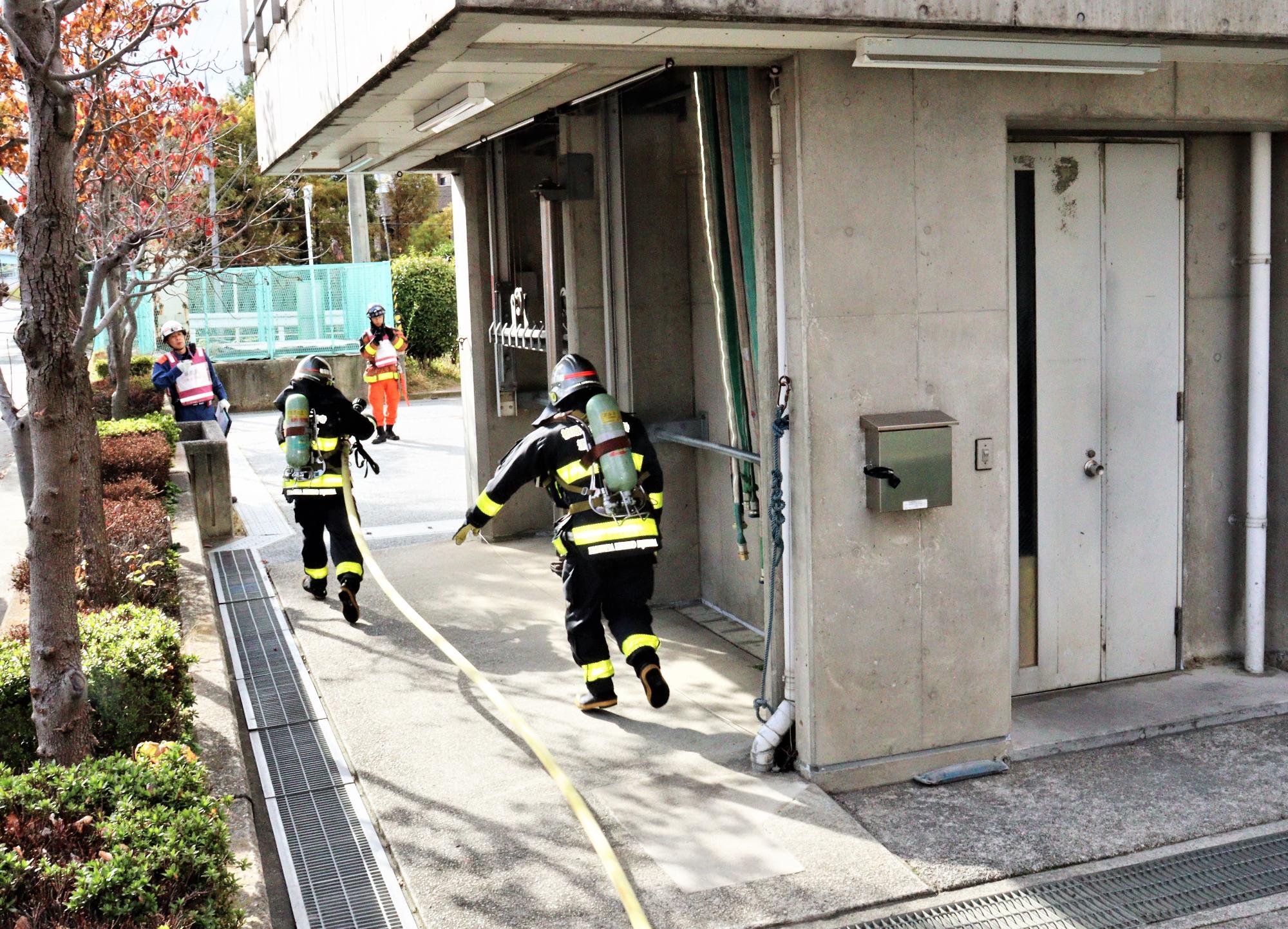 隊長と放水隊員1名が隣接する建物への延焼防止のために消防ホースを携え駆け出している様子