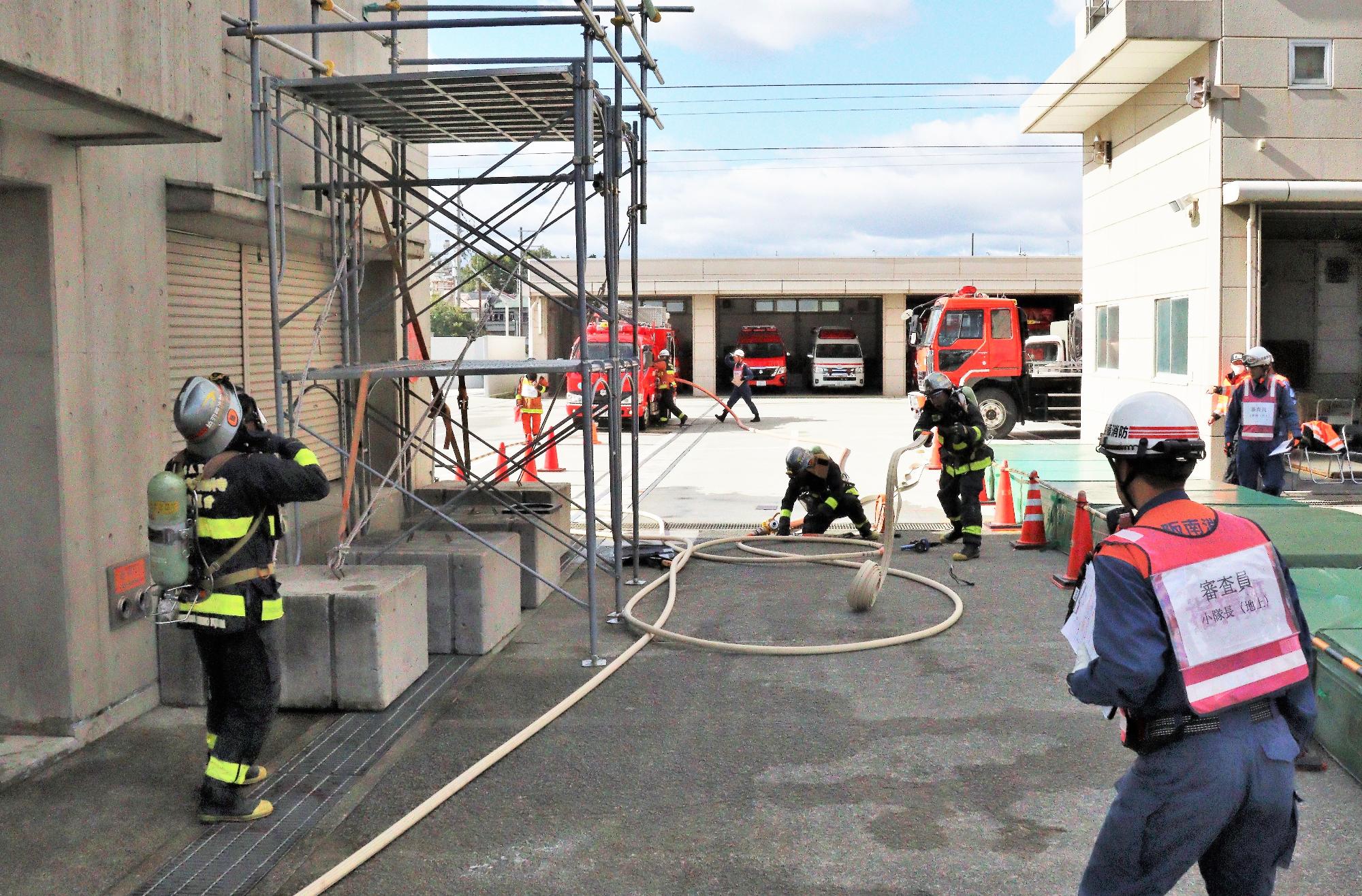 火災建物の玄関から3階の火災室へホースを延長するため地上で隊員がホースを延ばしている様子