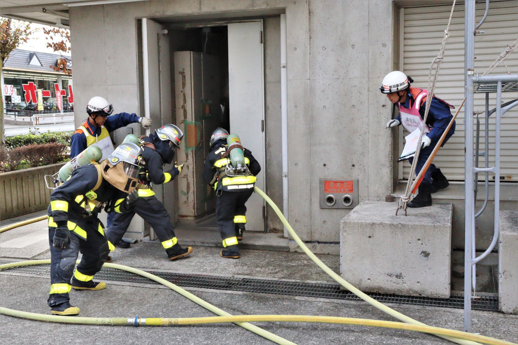 隊長と隊員2名が火災建物玄関から3階へ消防ホースを携えて進入している様子
