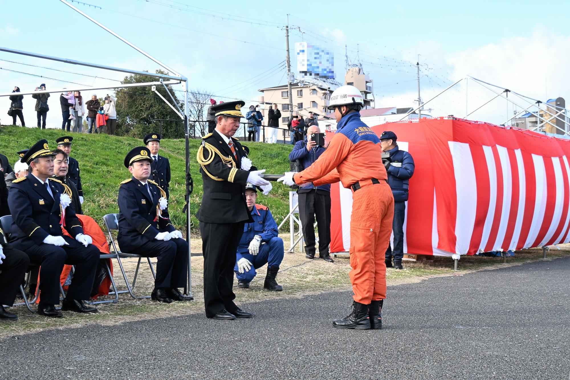 消防ヘリから投下された消防庁長官メッセージが救助隊員から柏原市消防団長に手渡される