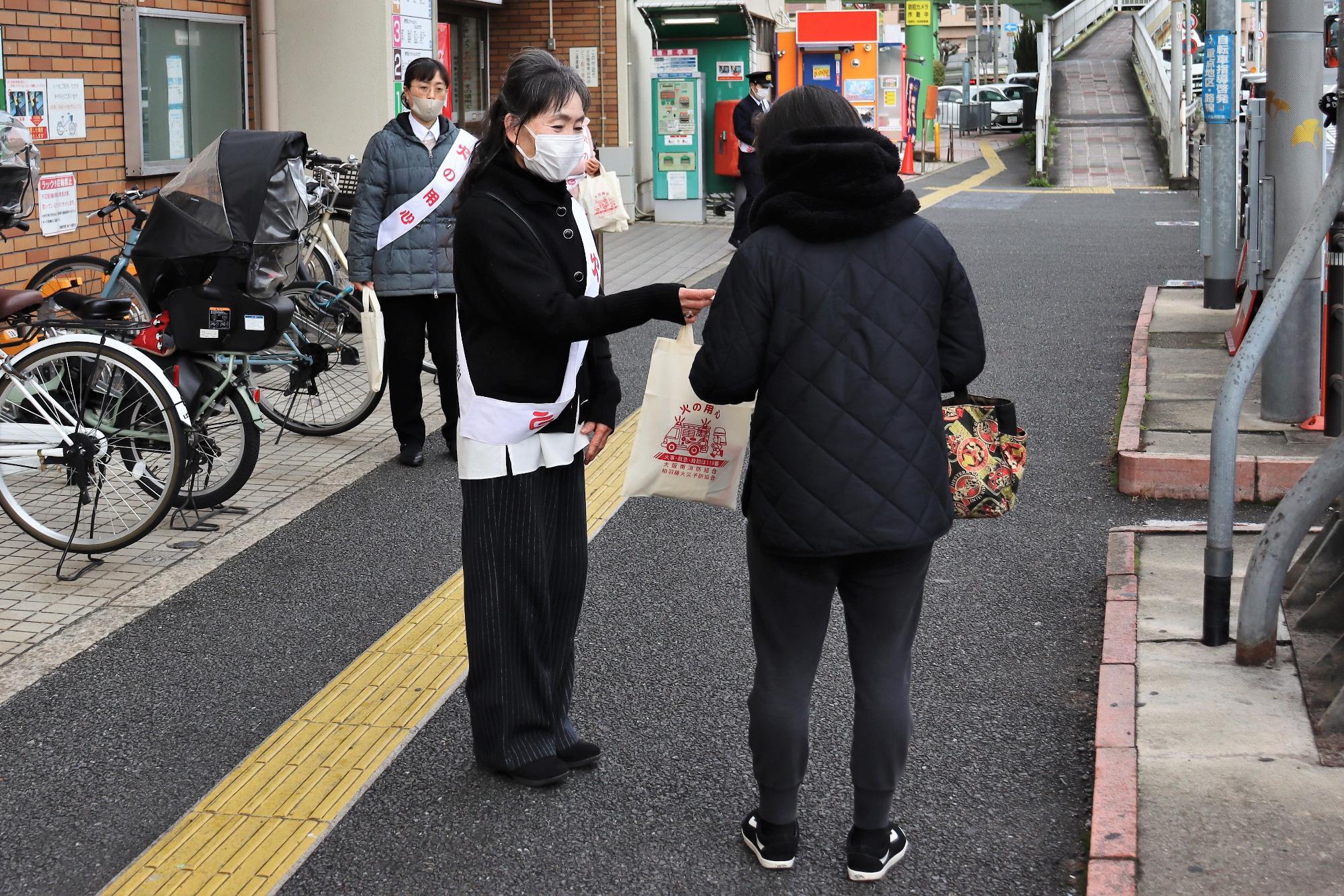 柏原市婦人防火クラブ会長が配布物を通行人に配布する様子
