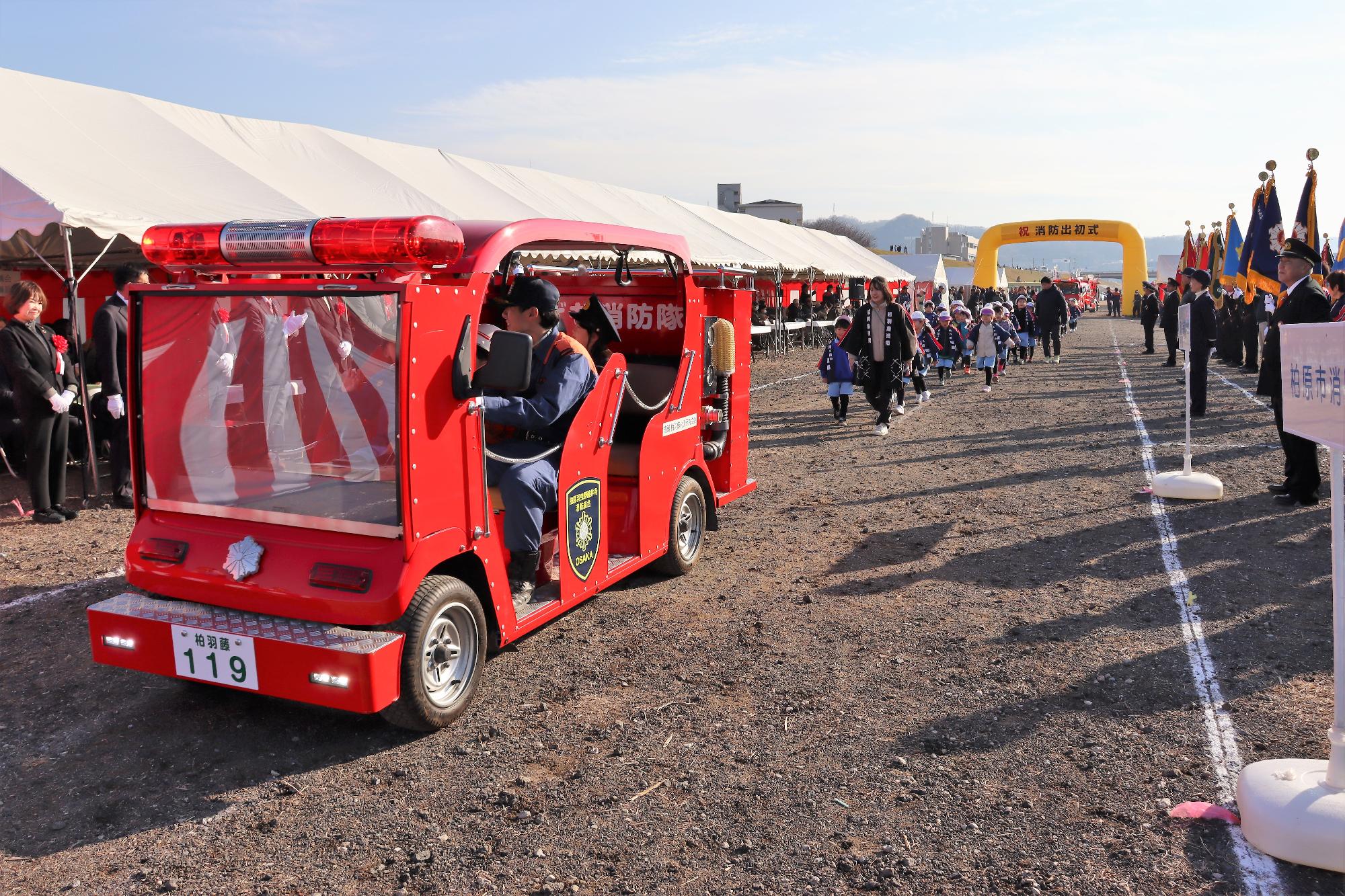 制服を着た幼稚園児がこども消防車に乗車しての行進の様子