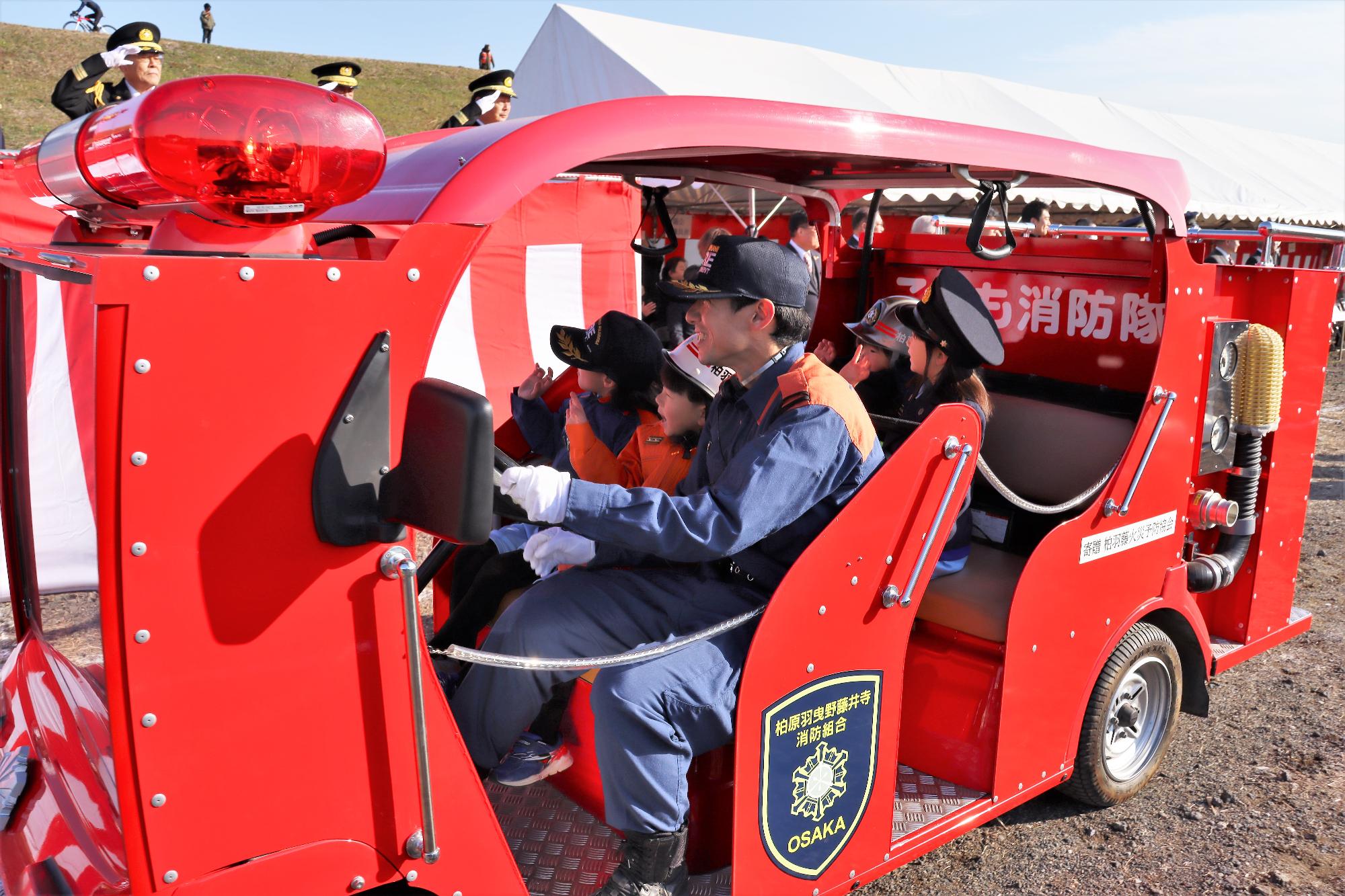 制服を着た幼稚園児がこども消防車に乗車しての行進の様子