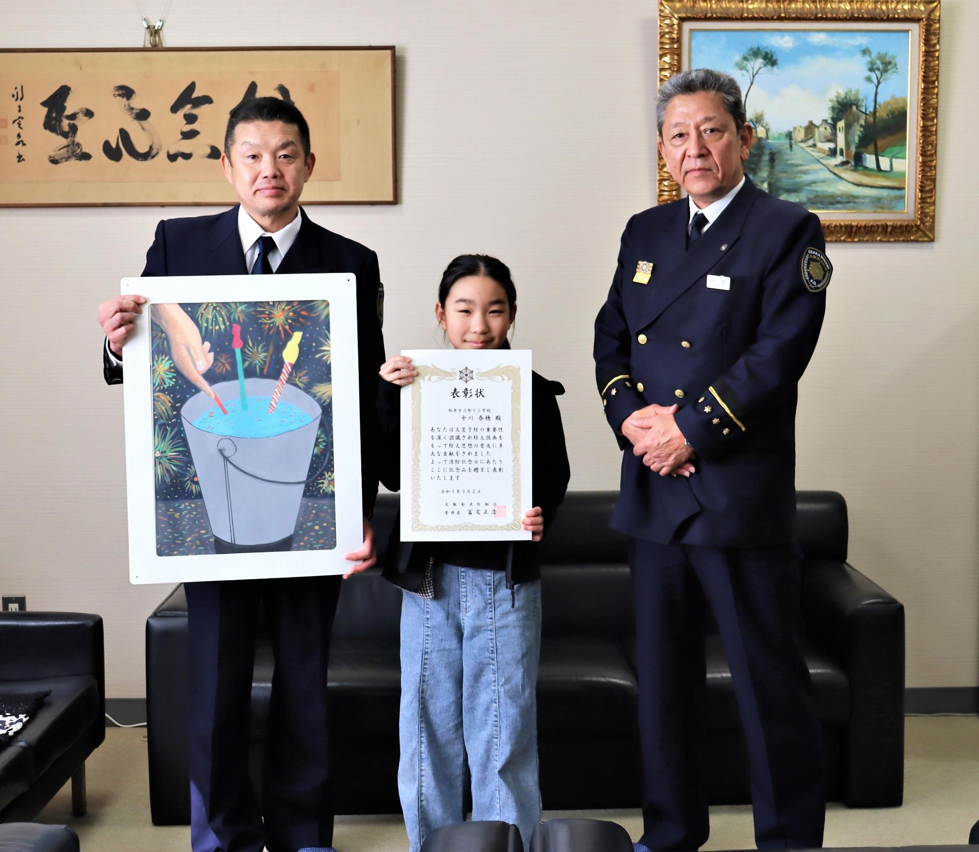左から防火図画の大阪府知事賞に入賞した中川さんと作品と小池消防局長の記念写真