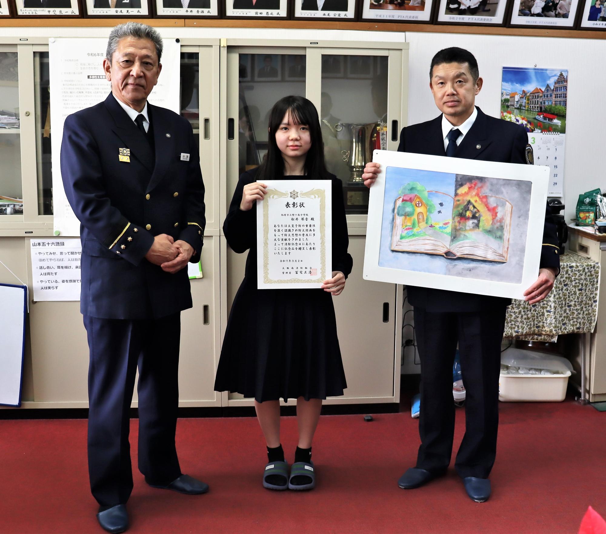 左から大阪南消防局小池局長、大阪府幼年少年女性等防火委員会会長賞に入賞した松井さんと作品の記念写真