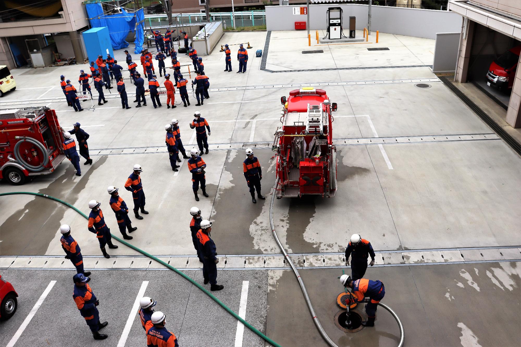 消防団員がグラウンドで消防車で消火栓から取水したり、ロープを取り扱う訓練をしている様子