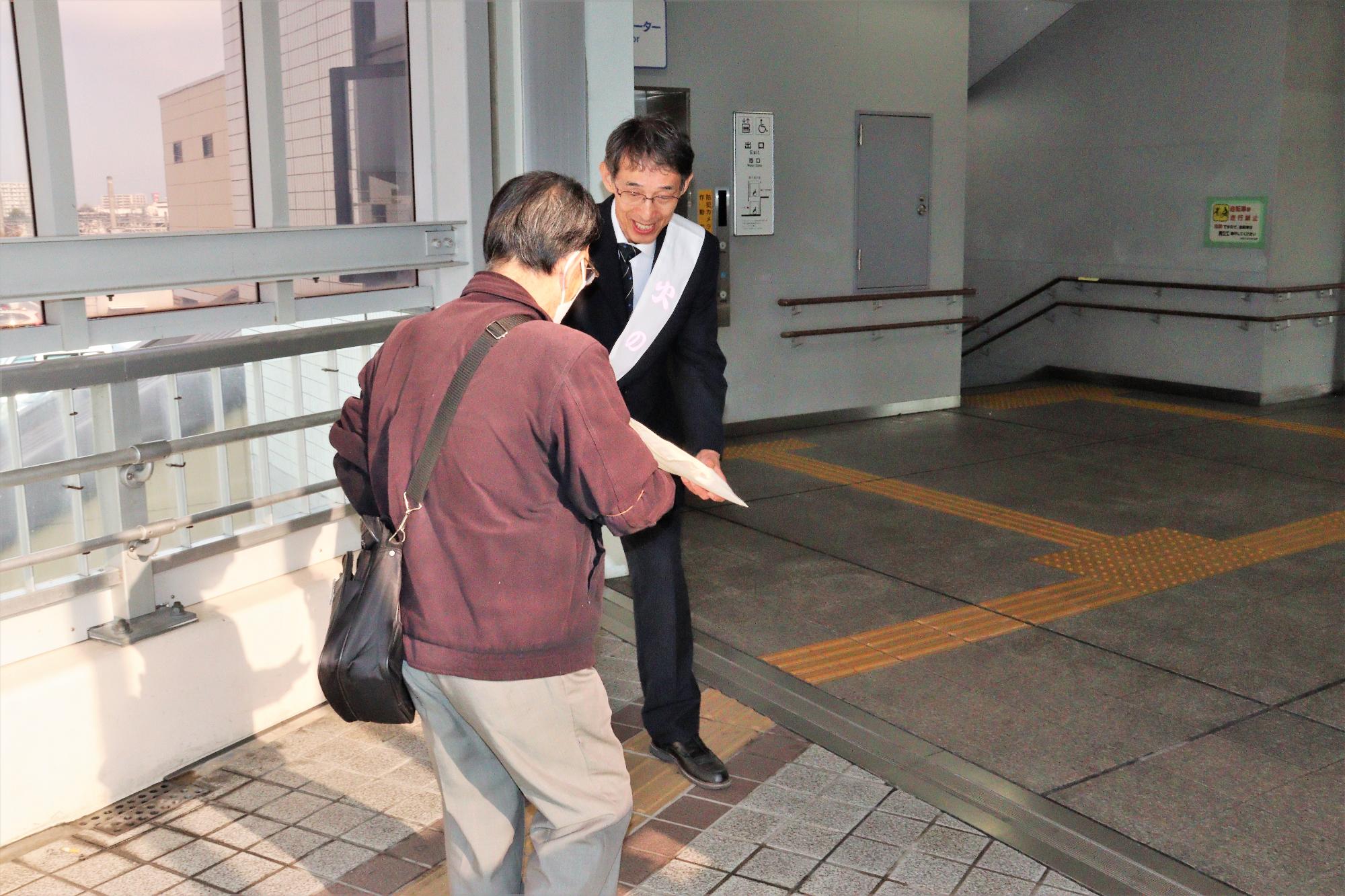 柏原駅構内にて火災予防協会長による火災予防啓発グッズの配布の様子